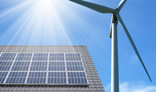 The roof of a home with solar panels, standing next to a wind turbine. Renewable Energy Concept.