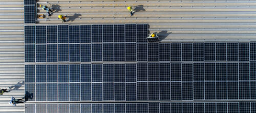 Workers installing a large group of solar panels on top of a roof.