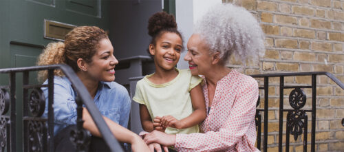 A multigenerational Black family sitting on front steps - a mother, daughter, and grandmother