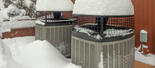 Heat pumps outside the home in the winter, covered in snow