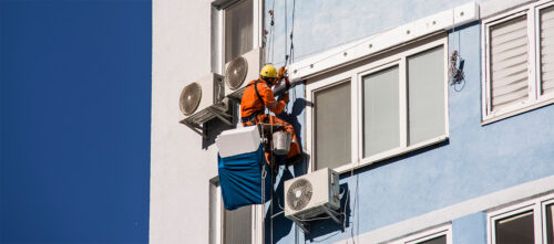 A technician repairing a heat pump on the exterior of a multifamily building.