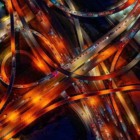 A Dallas highway interchange at night, illuminated by yellow headlights and red taillights of vehicles.