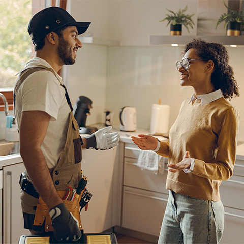 A young Black female homeowner discusses renovations with a contractor in her kitchen.