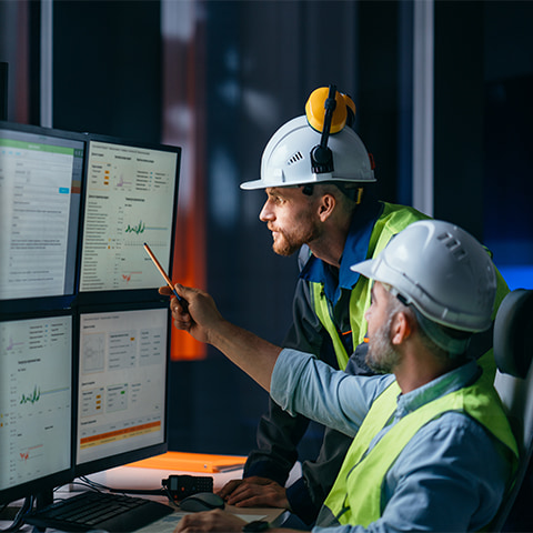 Two white male engineers examining data on a computer, using software systems to monitor and optimize manufacturing