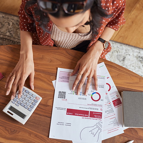 An aerial shot of a woman paying a utility bill on a kitchen table.