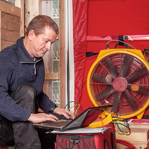 A middle-aged white male contractor conducts an energy assessment using a blower door.