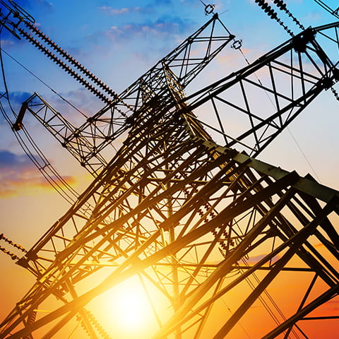 An electricity pylon as viewed from below with a sunset in the background