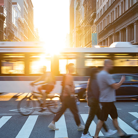 A busy city intersection on a sunny day. People walk, bike, and travel by bus.