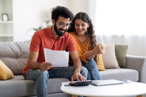 An Indian couple sitting on a couch looking at energy bills.